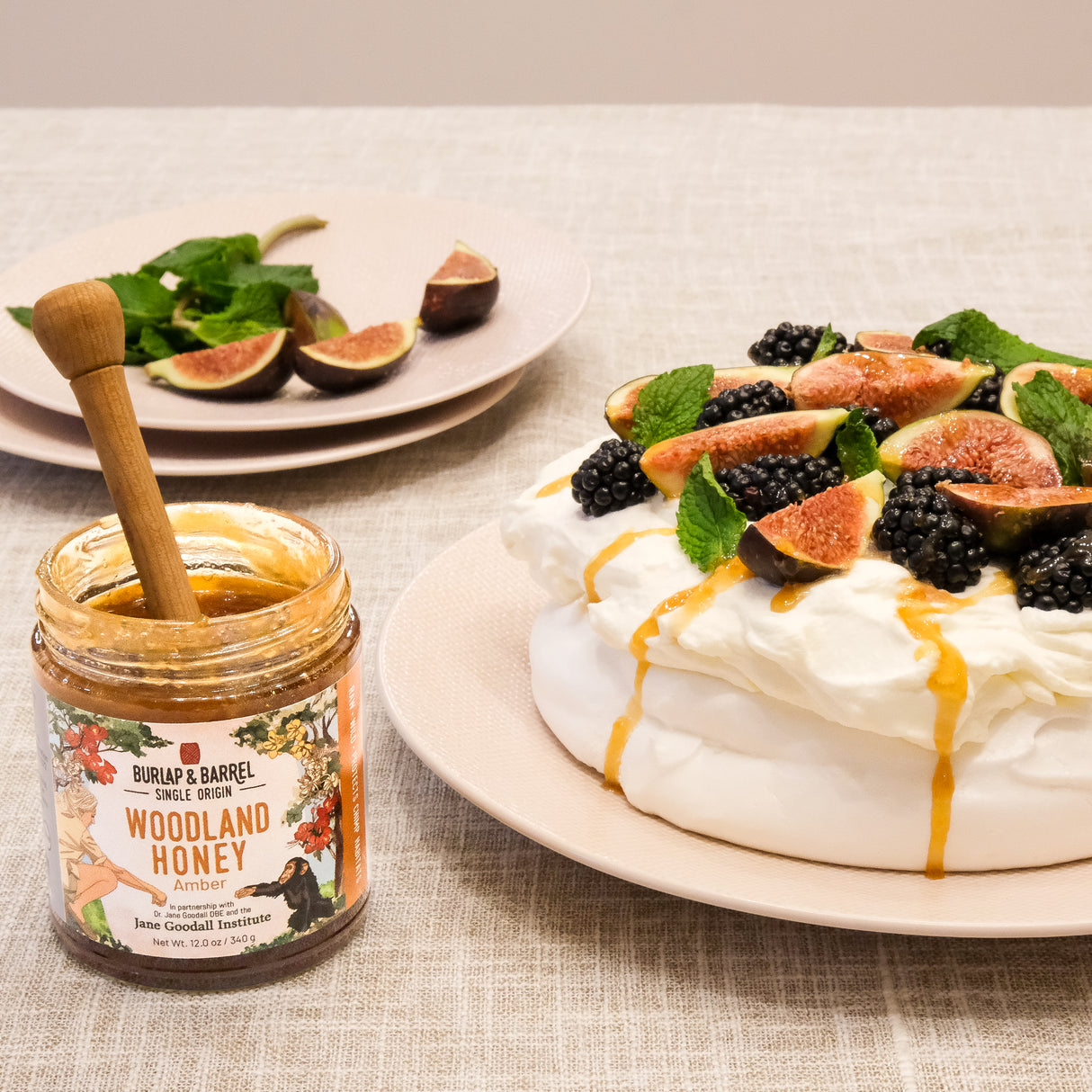 Meringue dessert with figs and blackberries on a plate next to a jar of Burlap & Barrel Amber Woodland honey.