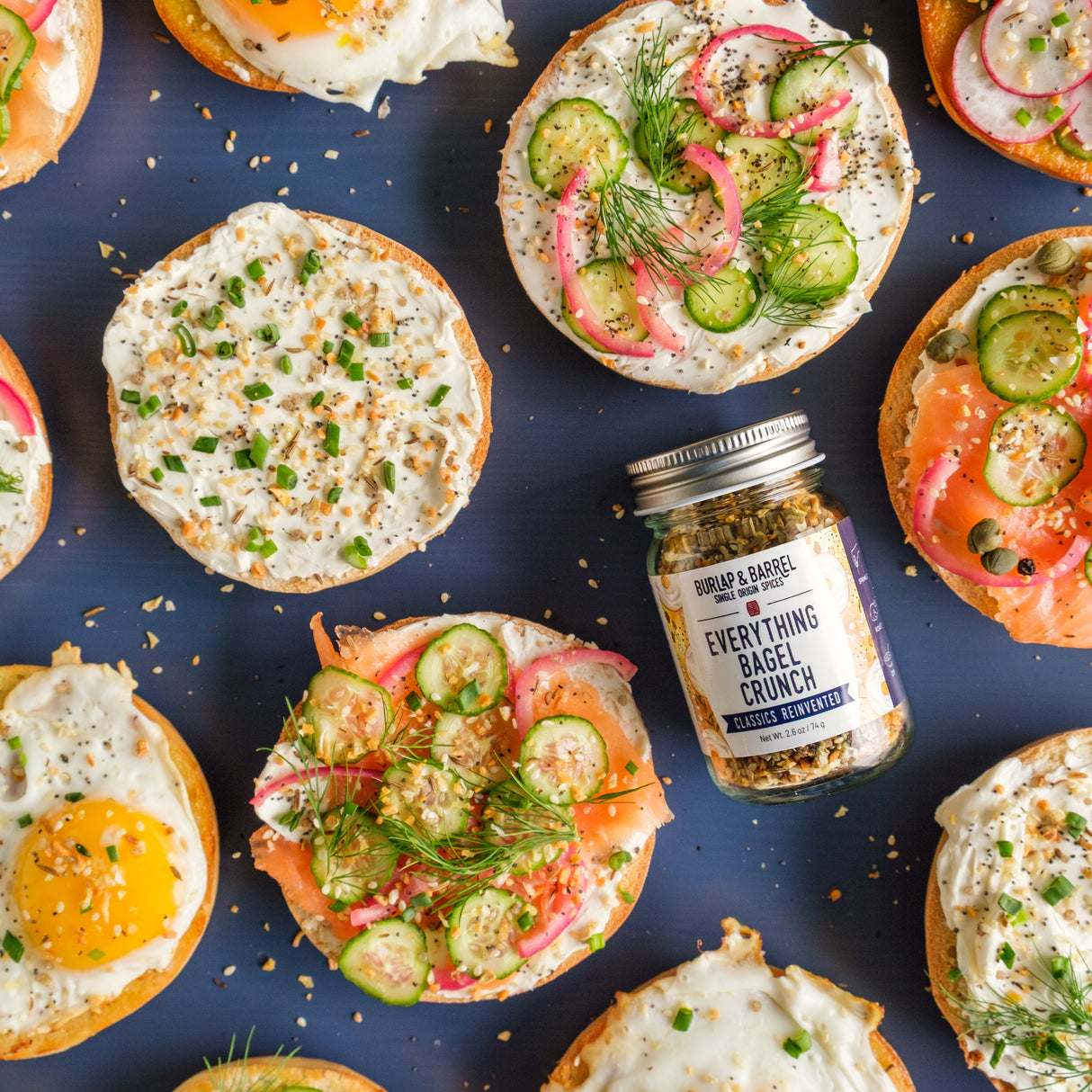 Assorted bagel toppings with a jar of everything bagel seasoning on a blue background