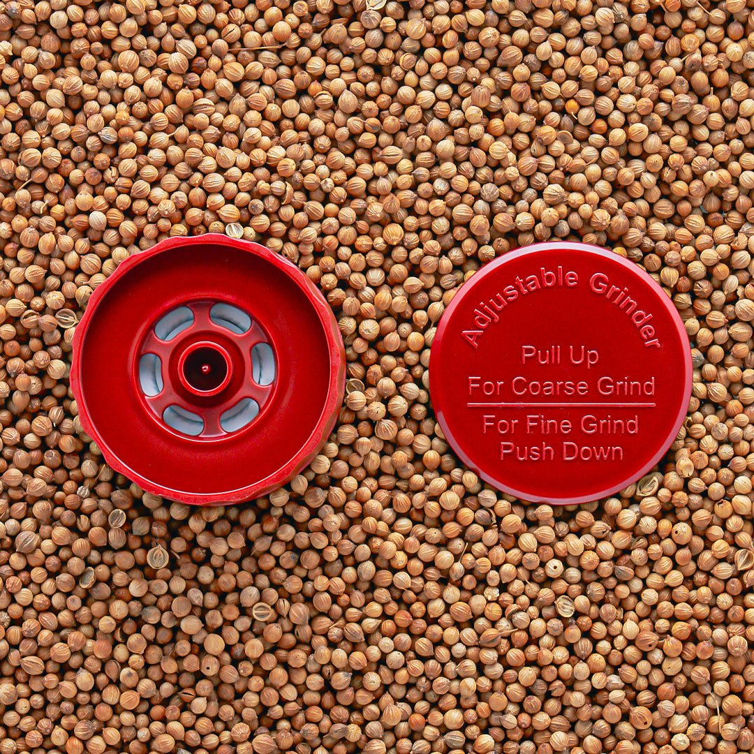 A red adjustable grinder top placed on a background of seeds, with instructions 'Pull Up For Coarse Grind' and 'Push Down For Fine Grind' visible.