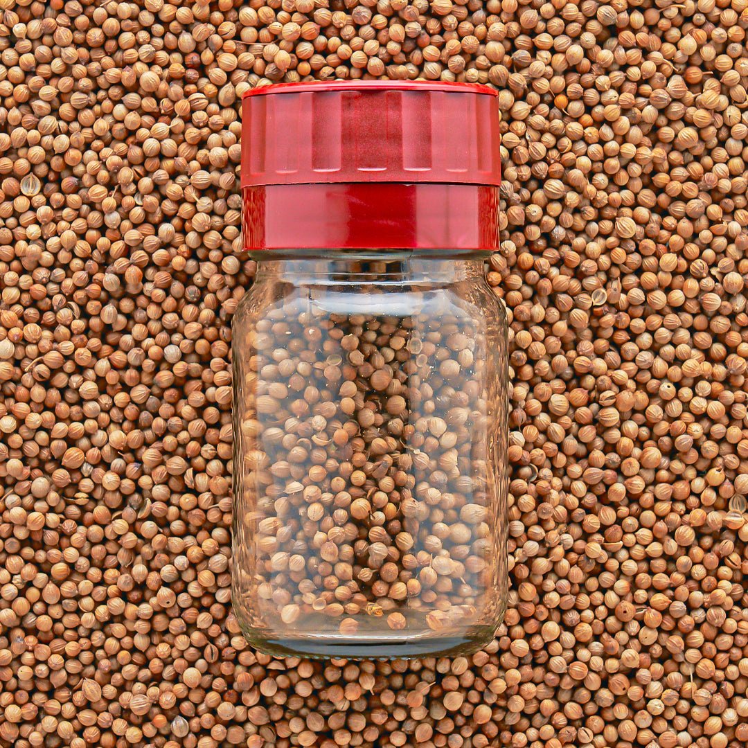 A clear jar with a red adjustable grinder top on top on a bed of seeds.