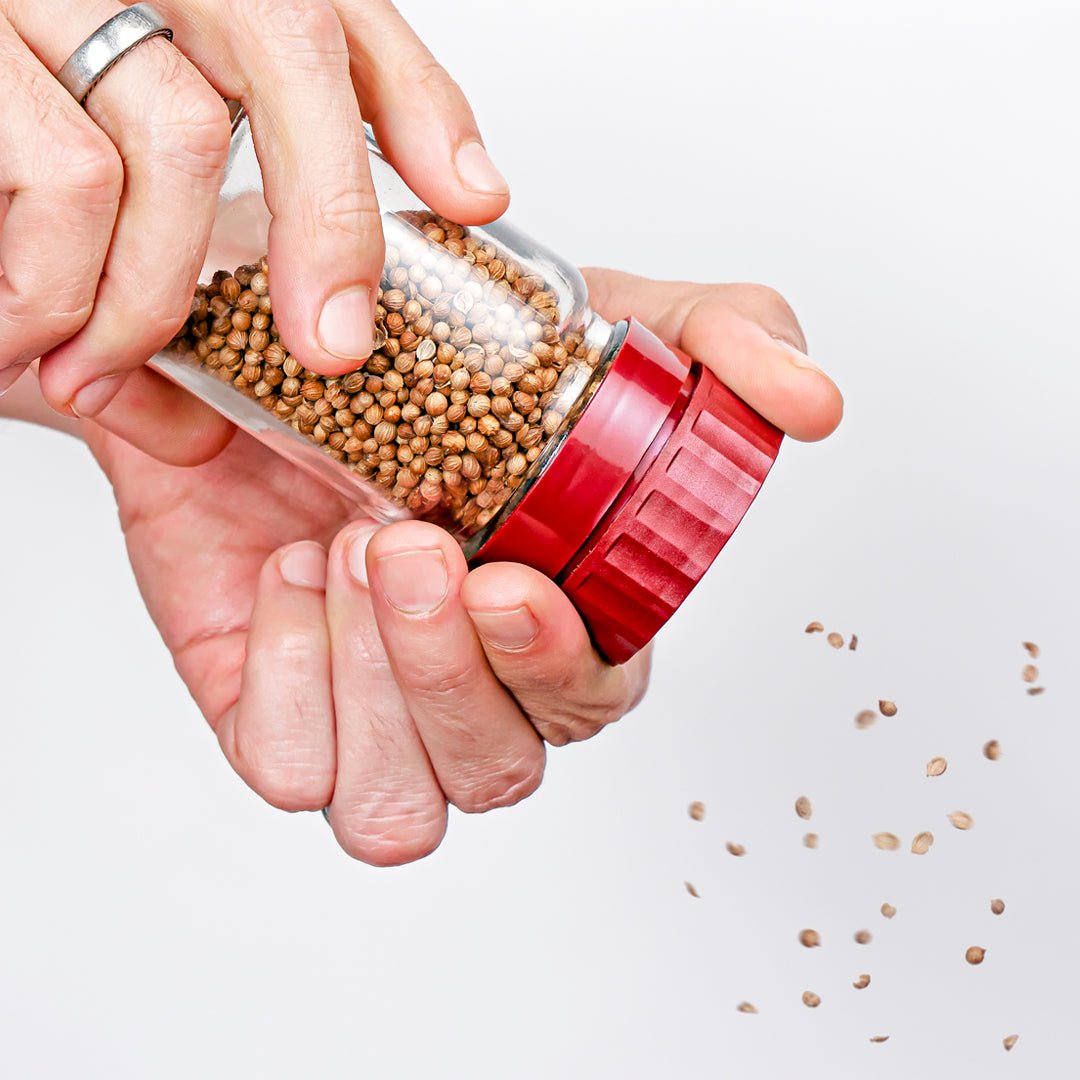 A closeup of two hands grinding spices from a jar with a burgundy Burlap & Barrel removable grinder-top.