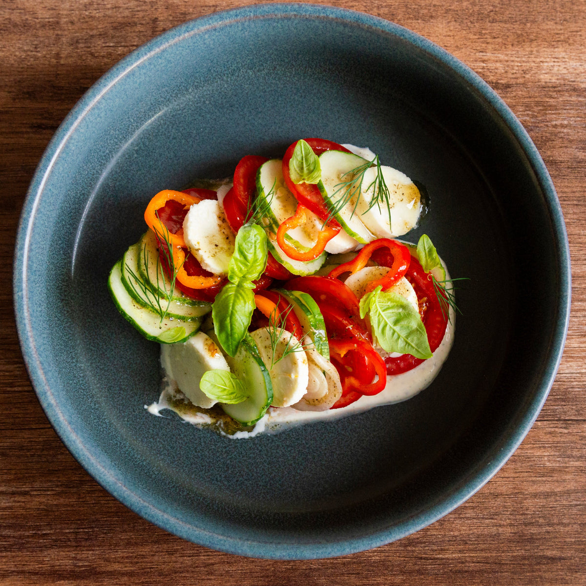 Fresh mozzarella with roasted peppers, cucumber, basil, and dill on blue plate