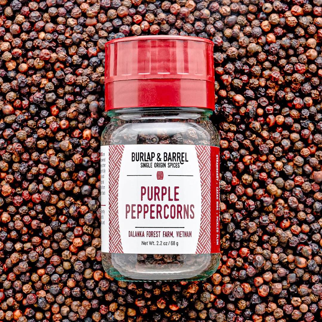 Burlap & Barrel Purple Peppercorns jar with red grinder lid on peppercorn background