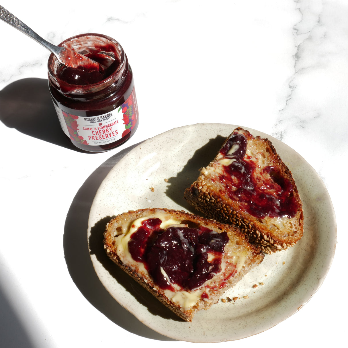 Two slices of toast with cherry preserves on a plate next to a jar of cherry preserves.