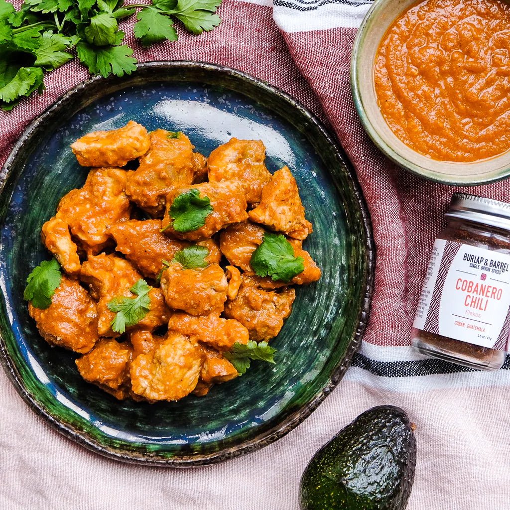 Cobanero chili chicken on blue-green plate with cilantro, chili paste, and avocado.