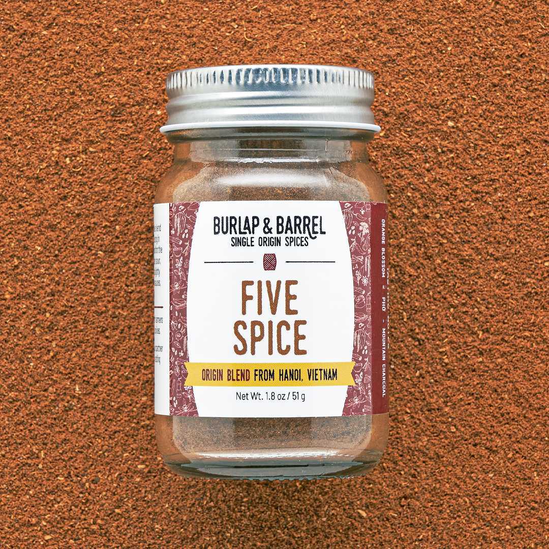 A glass jar with a metal lid labeled 'FIVE SPICE' from Burlap & Barrel on an orange textured background.
