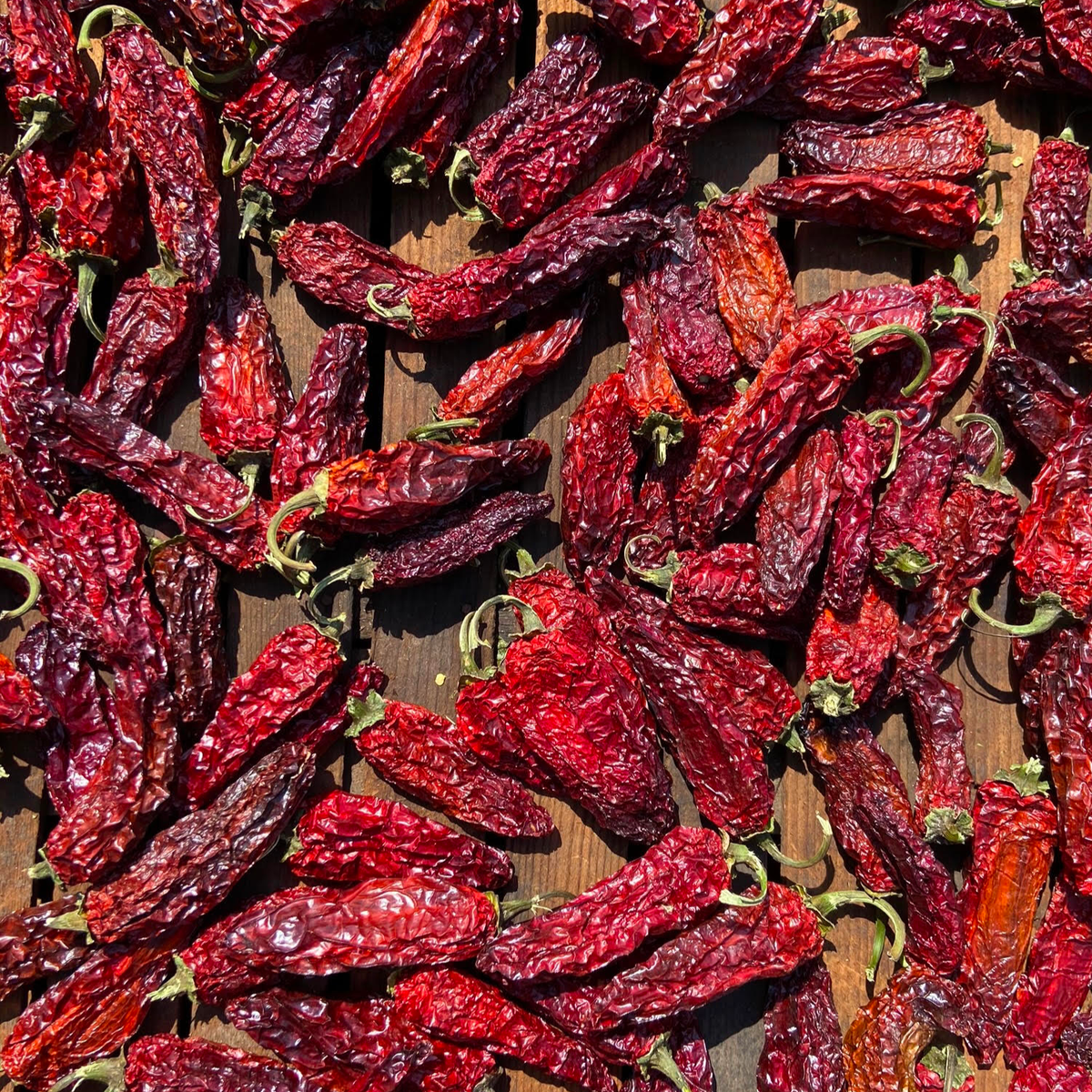 Dried red chili peppers with green stems on wooden surface in sunlight