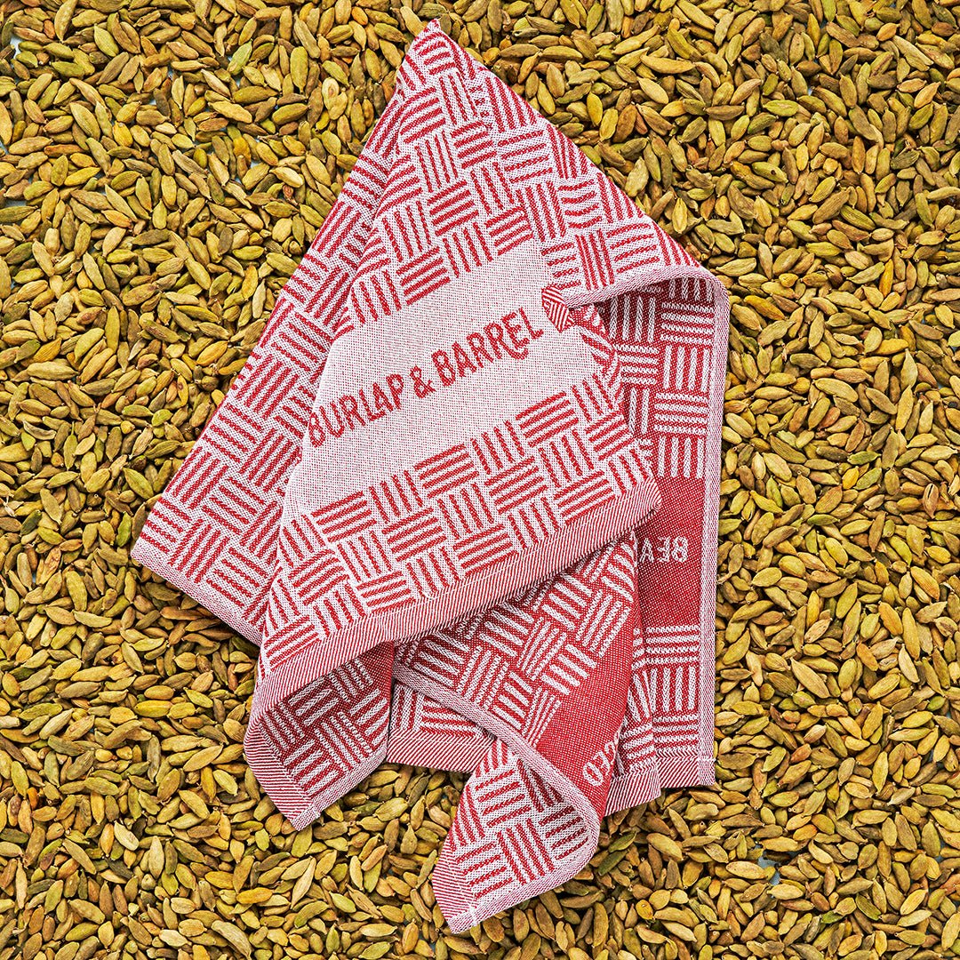 Red and white geometric patterned kitchen towel labeled ""Burlap & Barrel"" on cardamom pods