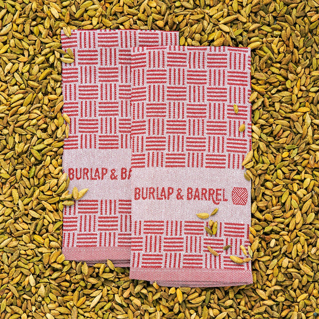 Red and white striped kitchen towel with ""BURLAP & BARREL"" branding on cardamom pods.