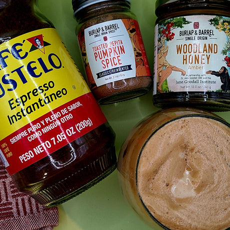  A top-down view of a frothy whipped coffee drink styled with a jar of Burlap & Barrel Toasted Pepita Pumpkin Spice and a jar of Woodland Honey Amber