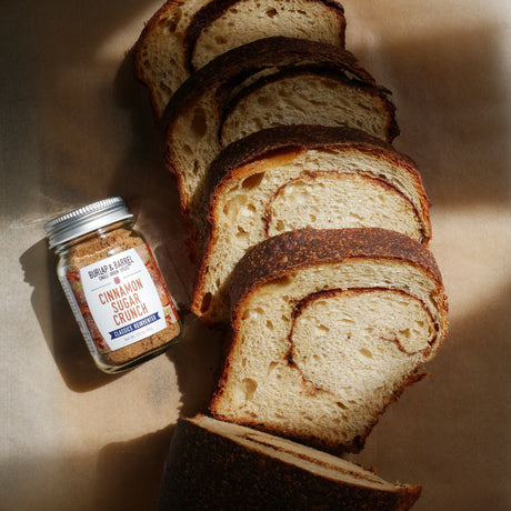lices of swirled cinnamon bread arranged on parchment paper next to a jar of Burlap & Barrel Cinnamon Sugar Crunch. Photo by Burlap & Barrel