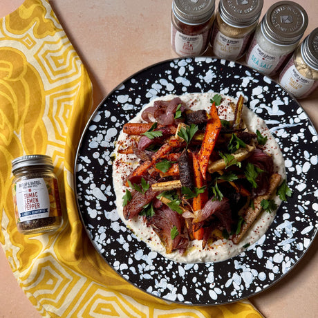 Photo by Clare Langan. Plate of roasted carrots and yogurt sauce. Next to it is a jar of sumac lemon pepper from Burlap & Barrel