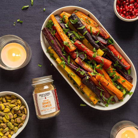 Roasted Carrots on an oval plate with a jar of Burlap & Barrel Navelina Orange Powder next to it on a gray background.