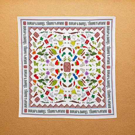 A multicolored, 100% cotton bandana with hand-drawn spice illustrations laid out flat on a surface.