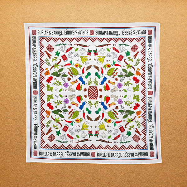 A multicolored, 100% cotton bandana with hand-drawn spice illustrations laid out flat on a surface.