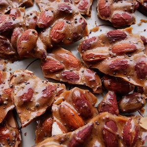Almond brittle with almonds and black mustard seeds on a white surface