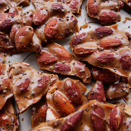 Almond brittle with almonds and black mustard seeds on a white surface