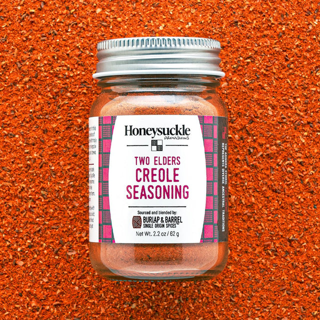 Two Elders Creole Seasoning by Honeysuckle Provisions in a glass jar with metal lid  spice blend background.