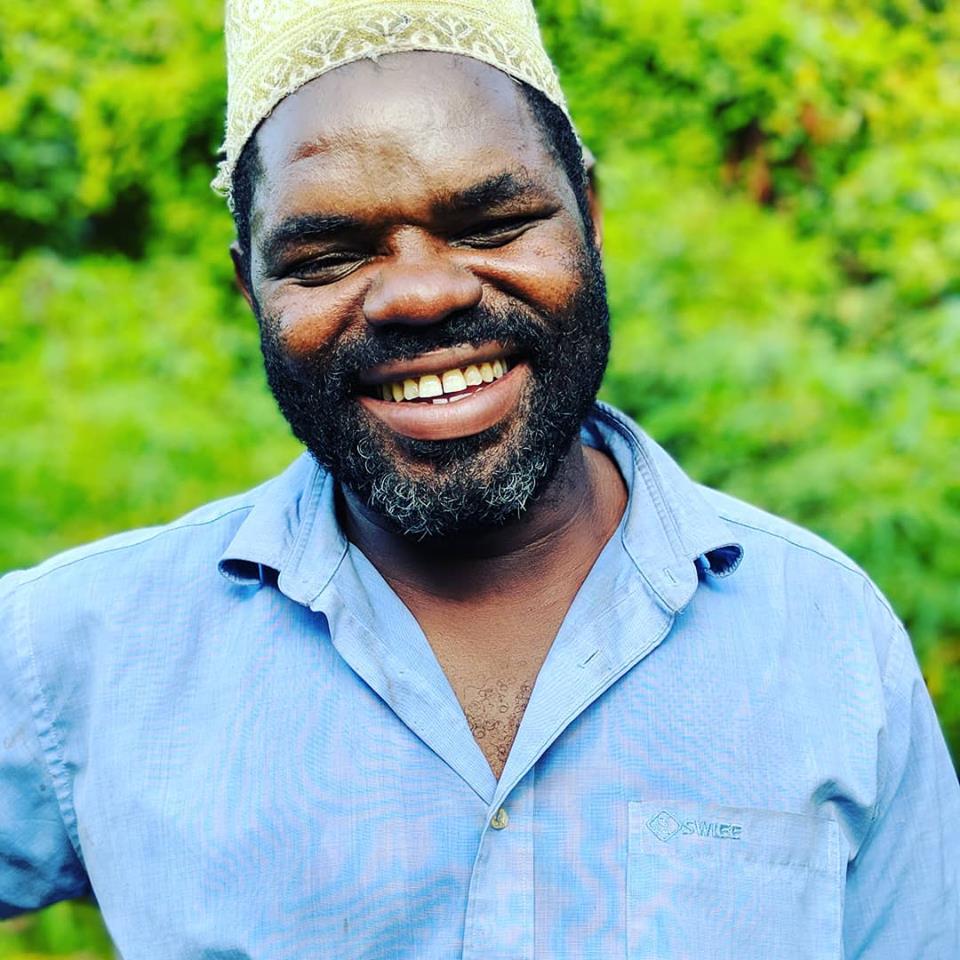 Partner Farmer, Bwana Mohammad in a blue shirt and yellow hat, smiling at the camera. 