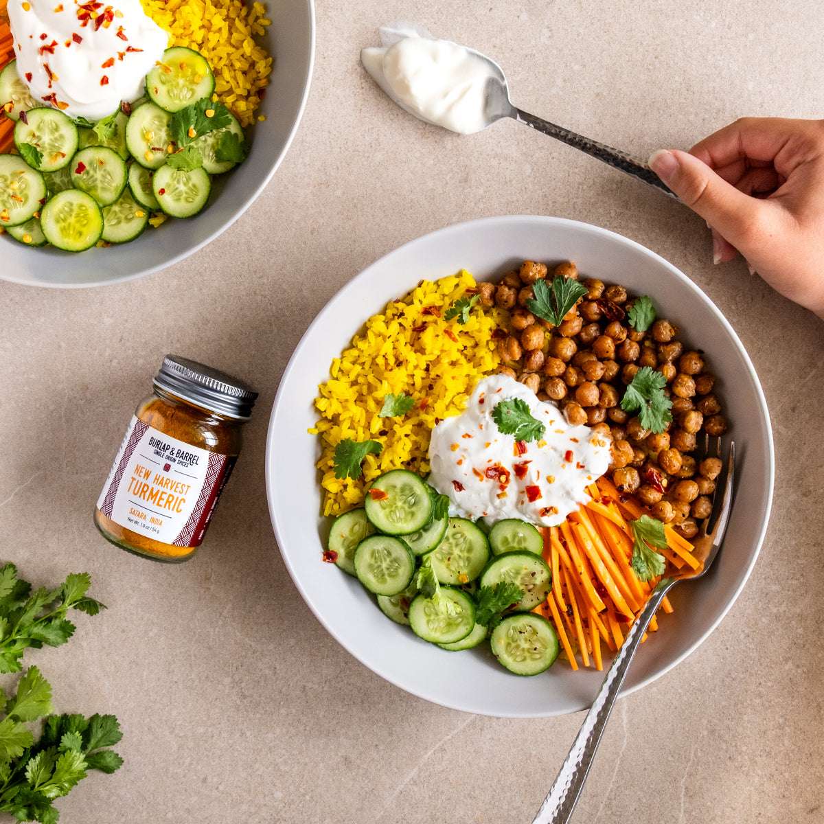 Bowl of salad with chickpeas, carrots, and cucumbers on a beige surface with a jar New Harvest Turmeric from Burlap & Barrel