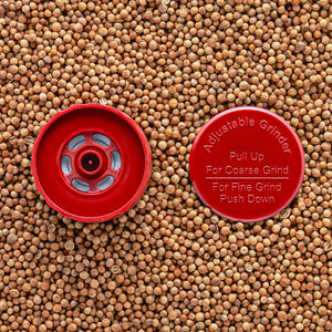 A red adjustable grinder top placed on a background of seeds, with instructions 'Pull Up For Coarse Grind' and 'Push Down For Fine Grind' visible.