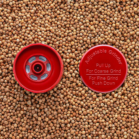 A red adjustable grinder top placed on a background of seeds, with instructions 'Pull Up For Coarse Grind' and 'Push Down For Fine Grind' visible.