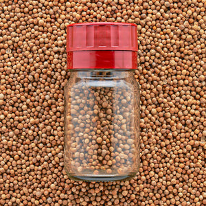 A clear jar with a red adjustable grinder top on top on a bed of seeds.