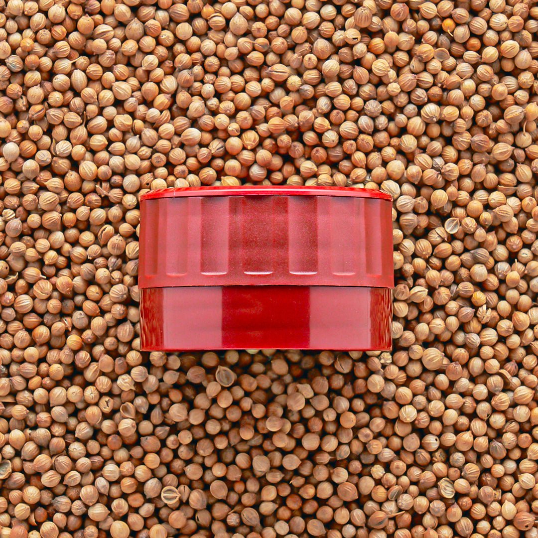 A red adjustable grinder-top that goes onto Burlap & Barrel jars on a bed of seeds.