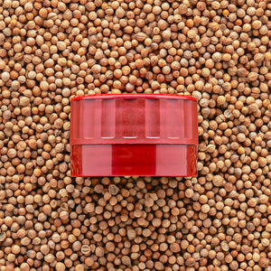 A red adjustable grinder-top that goes onto Burlap & Barrel jars on a bed of seeds.