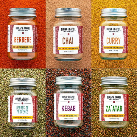 Six glass jars of Burlap & Barrel spice blends arranged in a 2x3 grid, each set against a textured background of the corresponding spice blend. The blends shown are Berbere, Chai, Curry, Herbes de Provence, Kebab, and Za'ATAR.