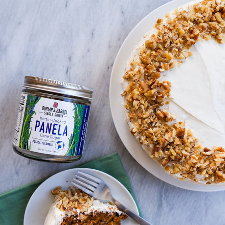 Jar of Burlap & Barrel Panela sugar next to a cake with a slice taken out on a marble surface.