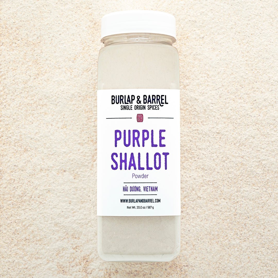 A container of Purple Shallot Powder by Burlap & Barrel, displayed on a background of beige powder.