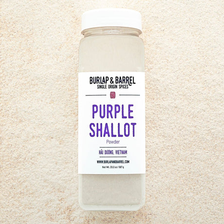 A container of Purple Shallot Powder by Burlap & Barrel, displayed on a background of beige powder.