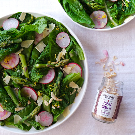 Green salad with radishes and a jar of purple shallots slices from Burlap & Barrel on a light background