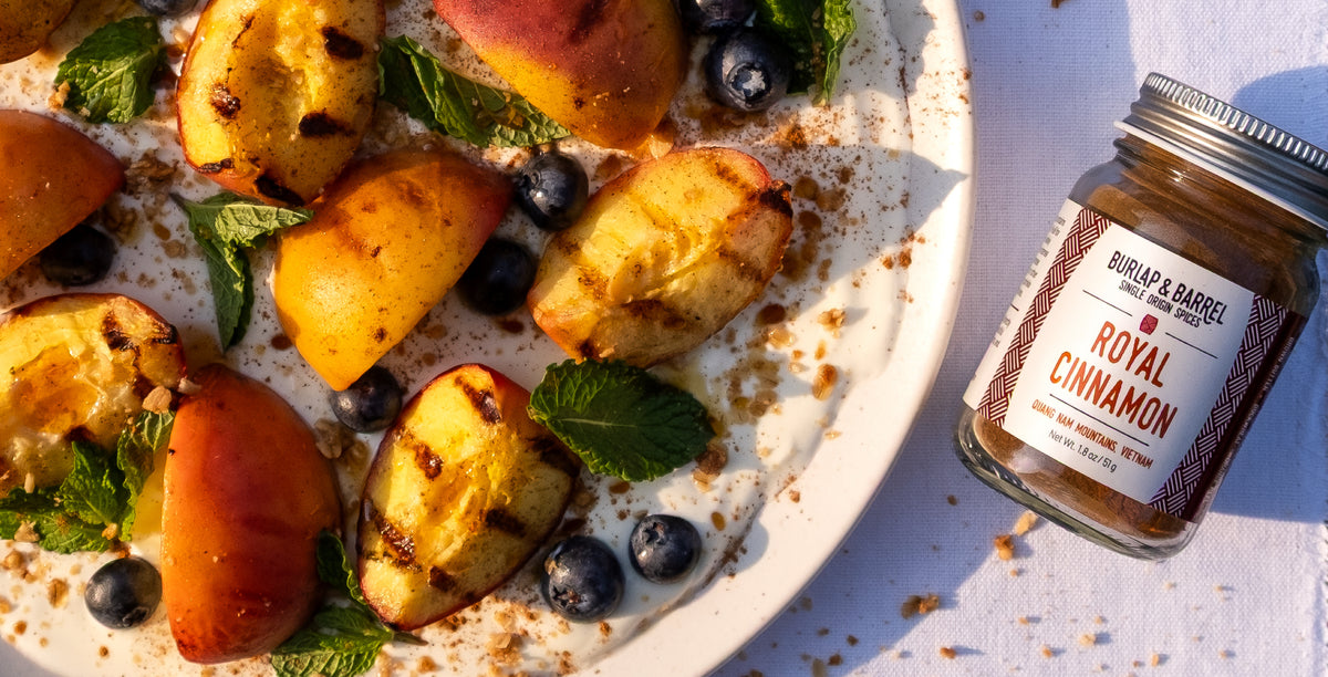 Dessert with peaches, blueberries, and mint leaves on a plate with a jar of Royal Cinnamon from Burlap & Barrel.