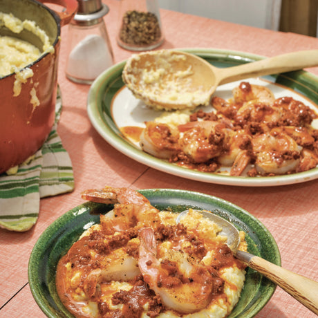 Two plates of food with shrimp and grits on a pink tablecloth.