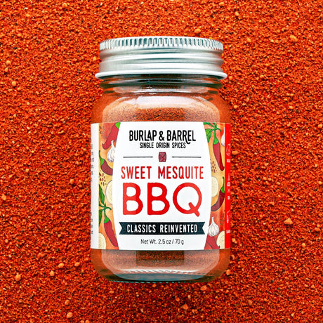 Jar of Burlap & Barrel Sweet Mesquite BBQ spice blend on a red background