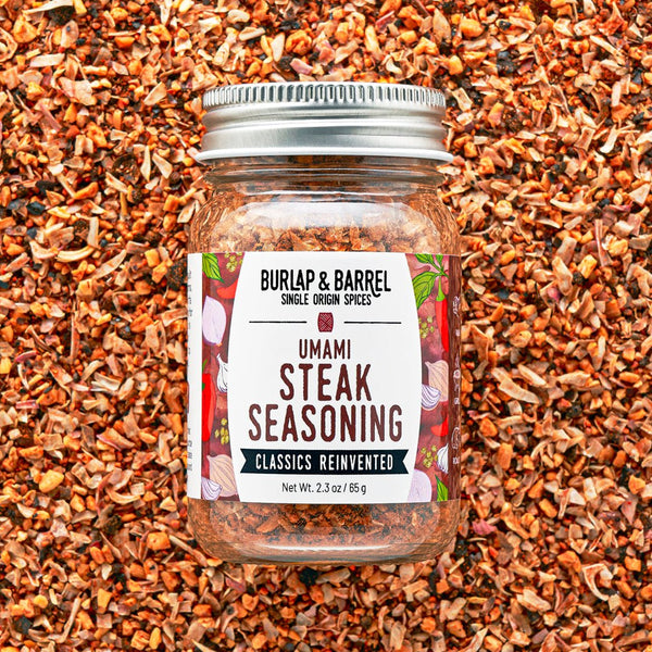 Jar of Burlap & Barrel Umami Steak Seasoning on a background of spices