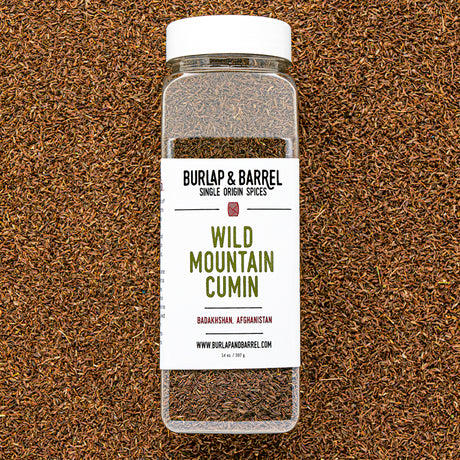 Plastic container of wild mountain cumin from Burlap & Barrel on a background of loose cumin seeds.