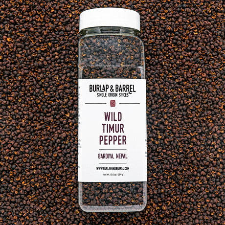 A bottle of Wild Timur Pepper by Burlap & Barrel, with the label showing the product name and origin, amidst loose peppers.