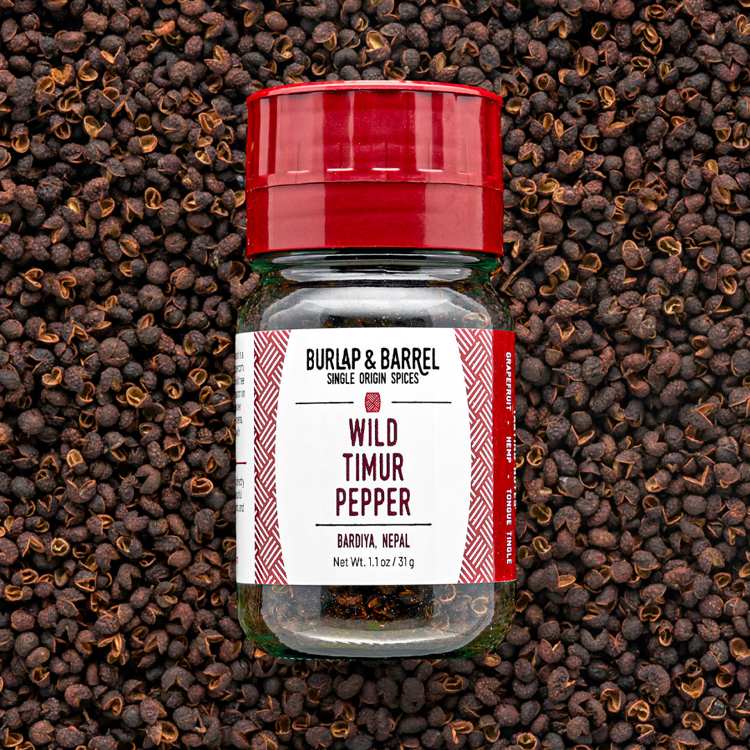 A bottle of Wild Timur Pepper by Burlap & Barrel, with the label showing the product name and origin, amidst loose peppers.