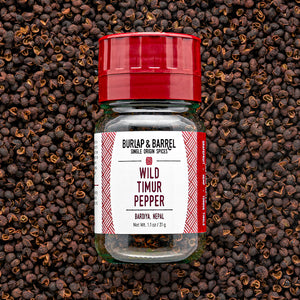 A bottle of Wild Timur Pepper by Burlap & Barrel, with the label showing the product name and origin, amidst loose peppers.