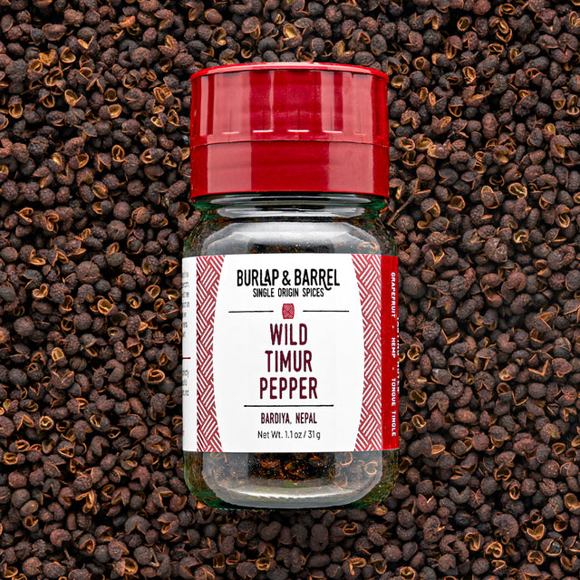 A bottle of Wild Timur Pepper by Burlap & Barrel, with the label showing the product name and origin, amidst loose peppers.