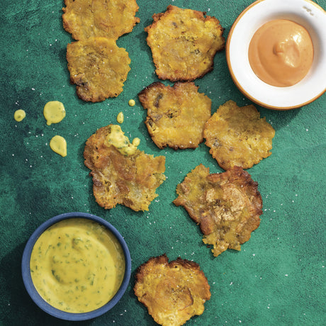 Fried green plantains with two dipping sauces on a green background