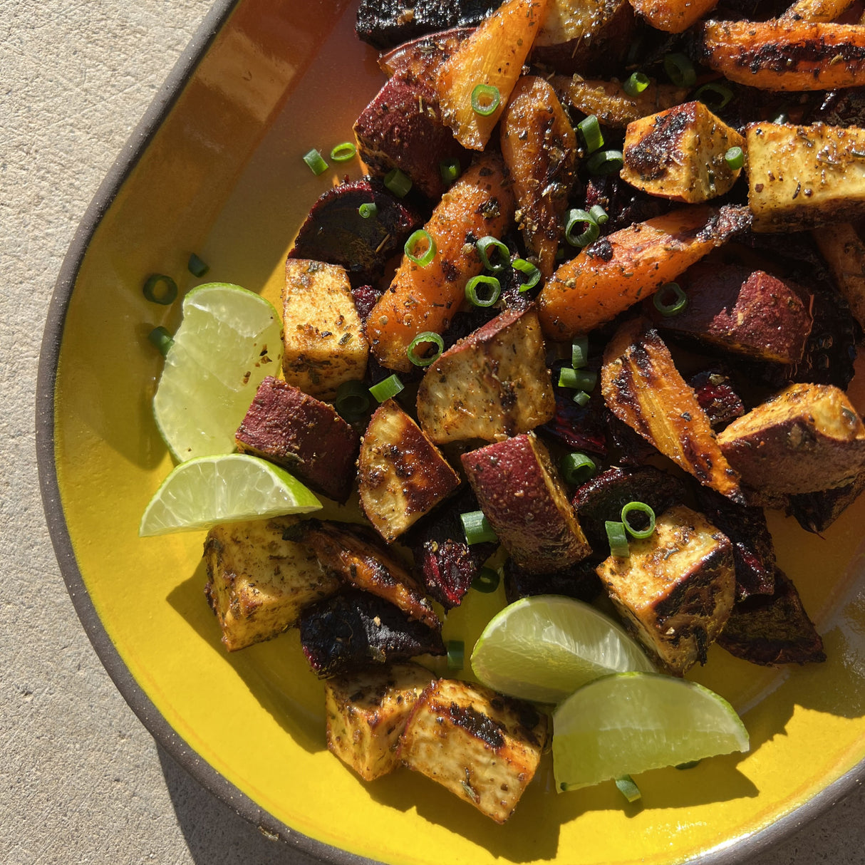 Roasted vegetables on a yellow plate with lime wedges