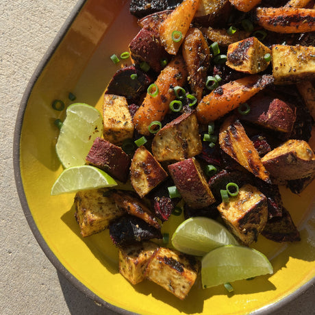 Roasted vegetables on a yellow plate with lime wedges