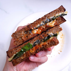 Hand holding a sandwich cut in half, with visible ingredients on a white plate.