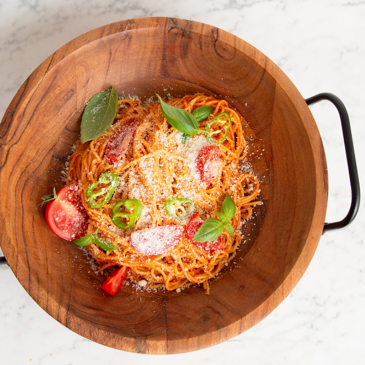Spaghetti with tomato sauce, grated cheese, sliced tomatoes, jalapeños, and basil in a wooden bowl