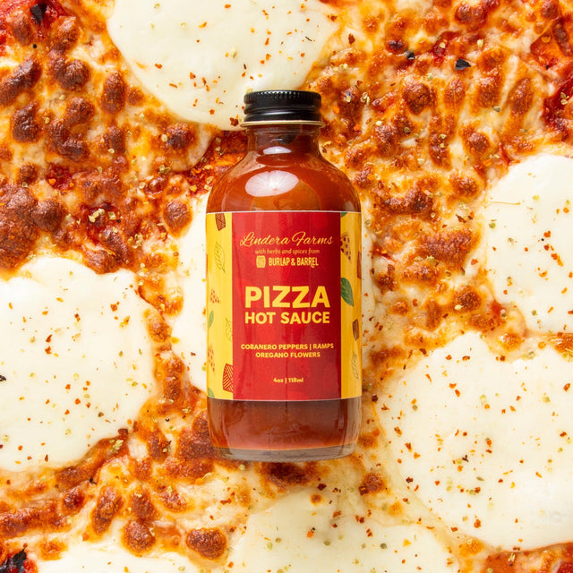 Lindera Farms Pizza Hot Sauce bottle on pepperoni pizza background with red and yellow label featuring Burlap & Barrel branding