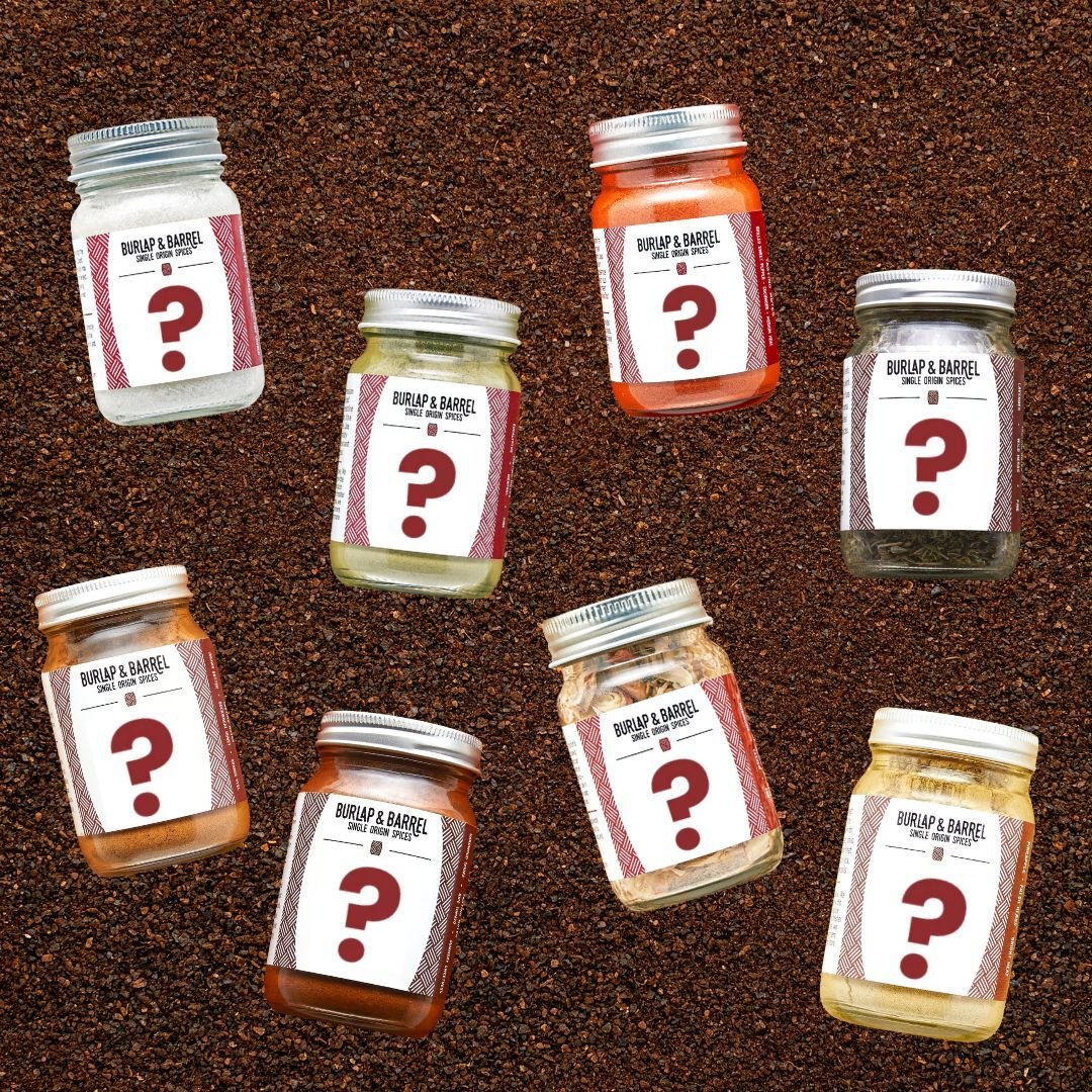 A collection of full-sized jars of spices with mystery labels, arranged on a bed of loose spices.